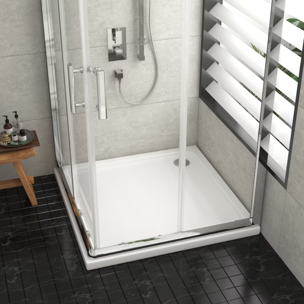 Glass shower enclosure with square shower tray, small wooden shelf with toiletries, and window with white blinds