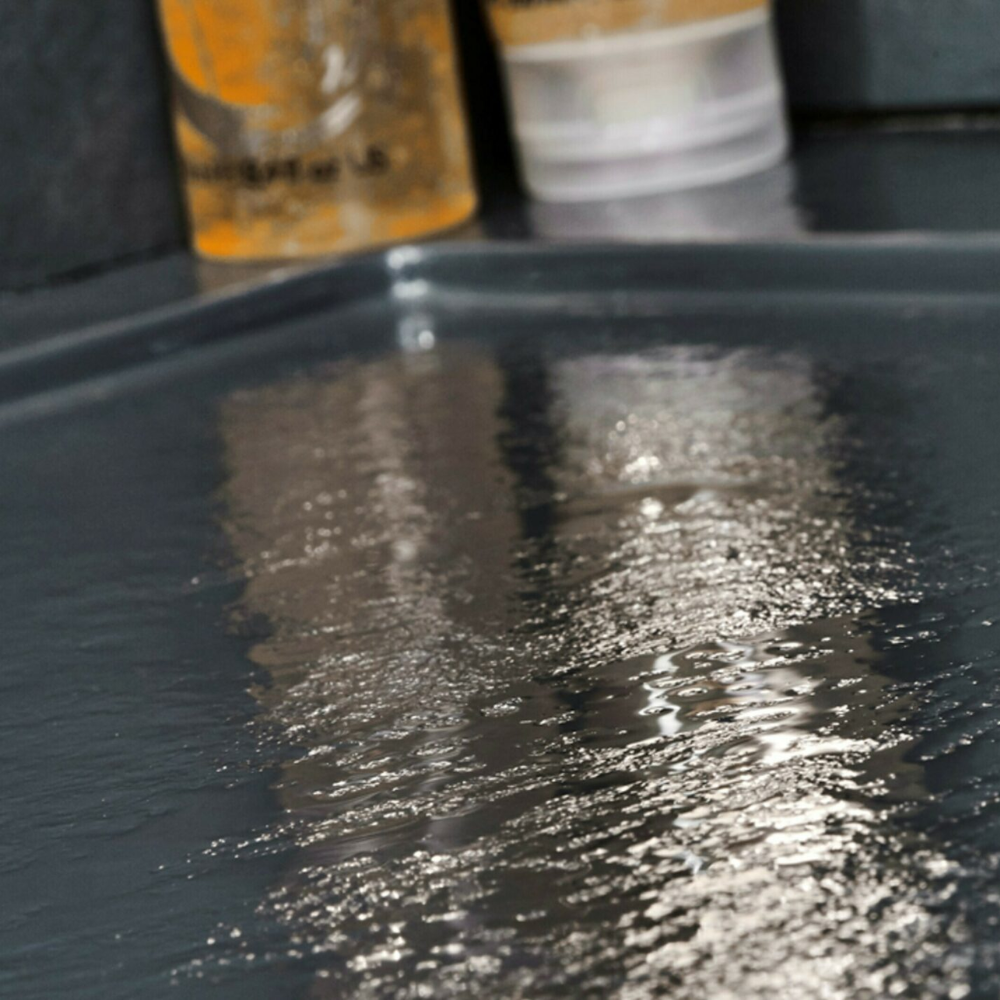 Wet black slate-effect shower tray with blurred bottles in background, surface glistening for fresh, clean look