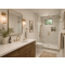 Wood vanity with marble top, brushed brass tapware, glass shower enclosure, indoor plants, and soft ambient lighting.