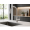 Stainless steel kitchen tap over large rectangular sink in a bright minimalist kitchen with plants and natural light.